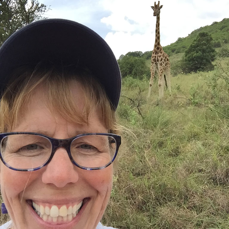 Michelle Salyers in Kenya with a giraffe right behind her